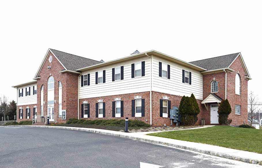 Two-story suburban brick and vinyl office building with white siding, multiple windows, and a parking area in front under an overcast sky.